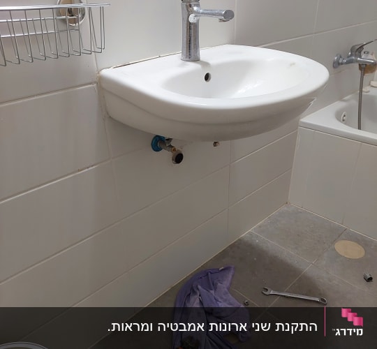 כיור לבן עם ברז מתכת על רקע אריחי קרמיקה